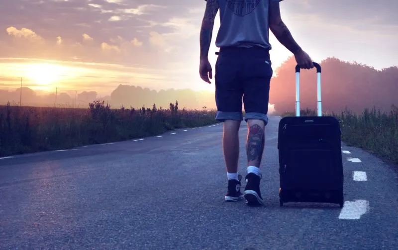 A photo of a man walking on the road with his luggage