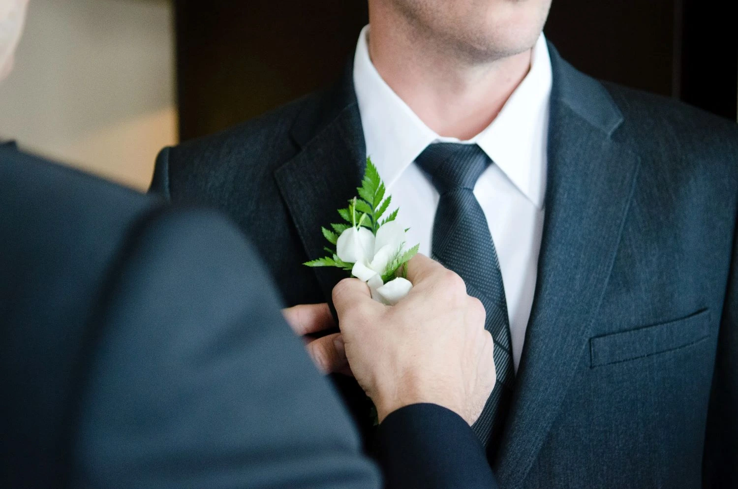 Bestman attaching a corsage to the groom's suit