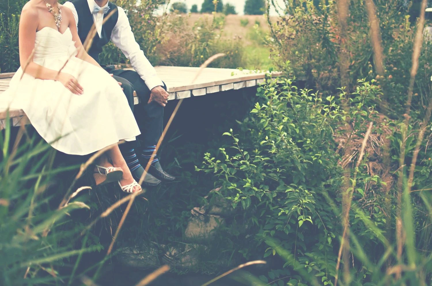 A couple in their wedding attire while sat on a bridge over a river